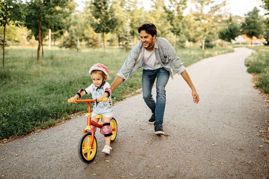 Ein Vater begleitet sein Kind beim Fahren auf dem Spielrad im Park.