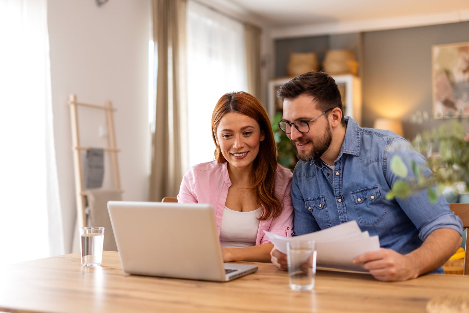 Zwei Menschen beim Arbeiten mit Laptop und Papieren in modernem Wohnraum