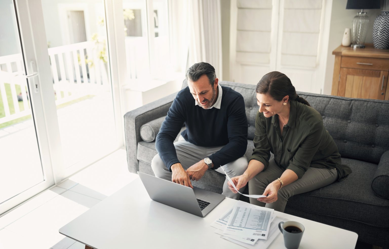 Zwei Personen arbeiten am Laptop mit Dokumenten in einem hellen Wohnzimmer aus dem Artikel Ihr Vermögen in besten Händen