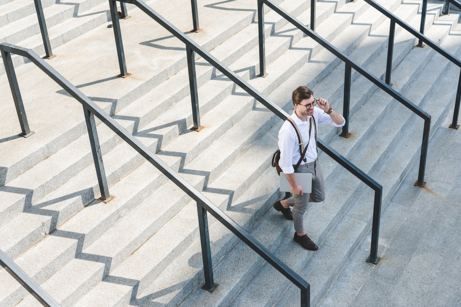 Junger Mann mit Laptop geht die Treppen einer modernen Bank hinunter.