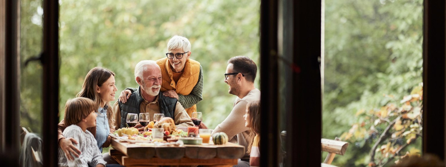Familie beim Frühstück in der Natur mit Blick auf Bäume und Fenster der BLKB