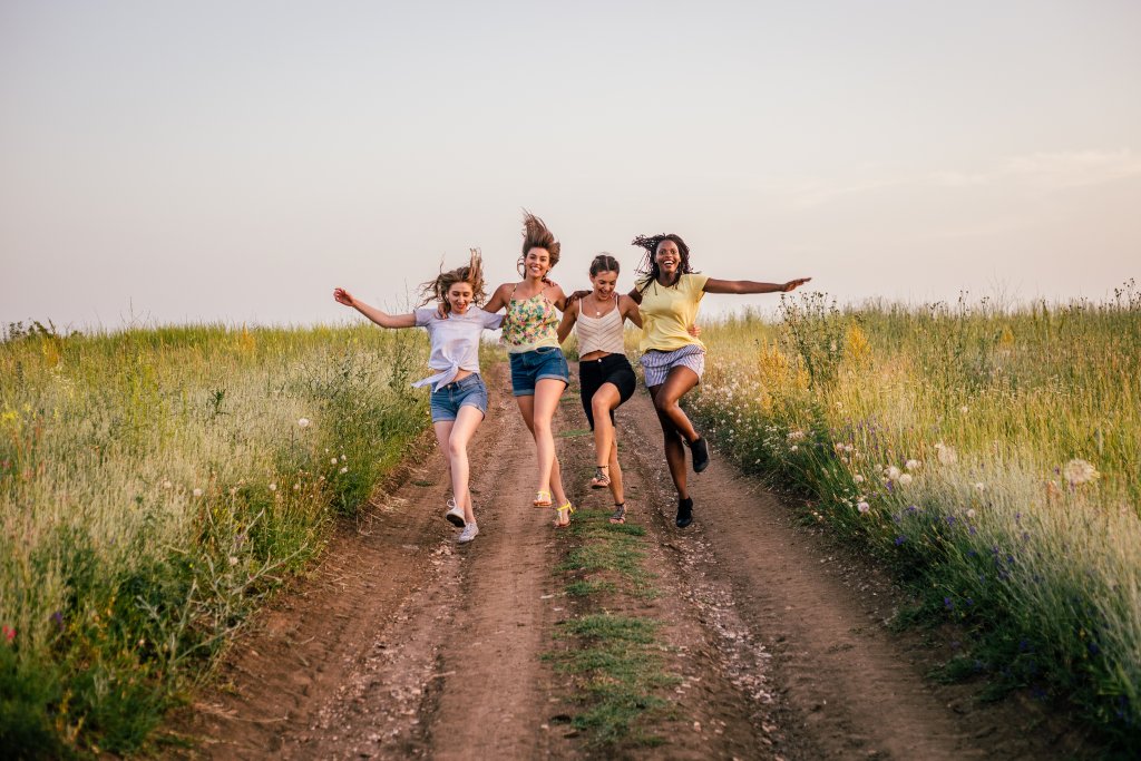 Vier Freunde spazieren fröhlich auf einem Feldweg in der Natur entlang.