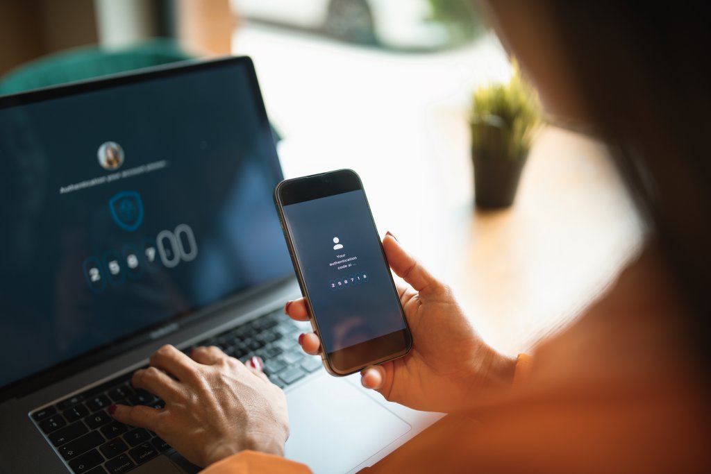 Person, die sich auf dem Laptop anmeldet, während sie das Smartphone zur Authentifizierung verwendet.