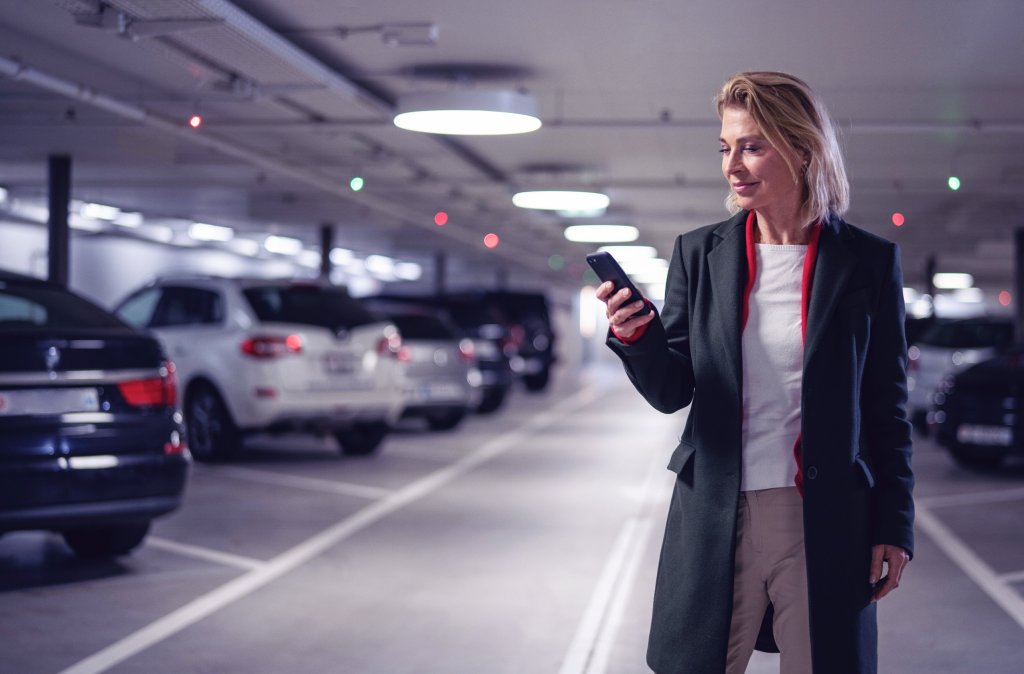 Eine Frau steht im Parkhaus und schaut auf ihr Smartphone.