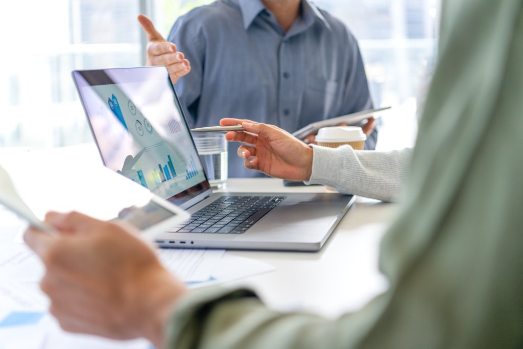 Menschen beraten sich an einem Tisch mit Laptop und Diagrammen zur Finanzplanung.