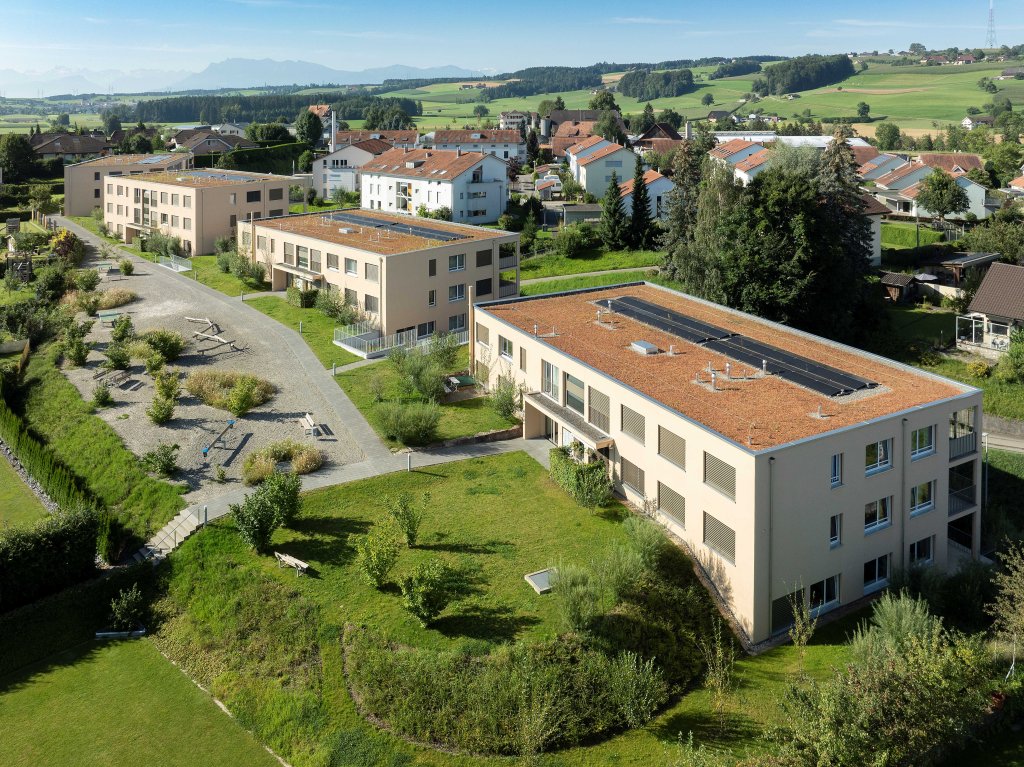 Mehrere moderne Gebäudekomplexe in einer grünen Landschaft mit Bäumen und Wegen. aus dem Artikel