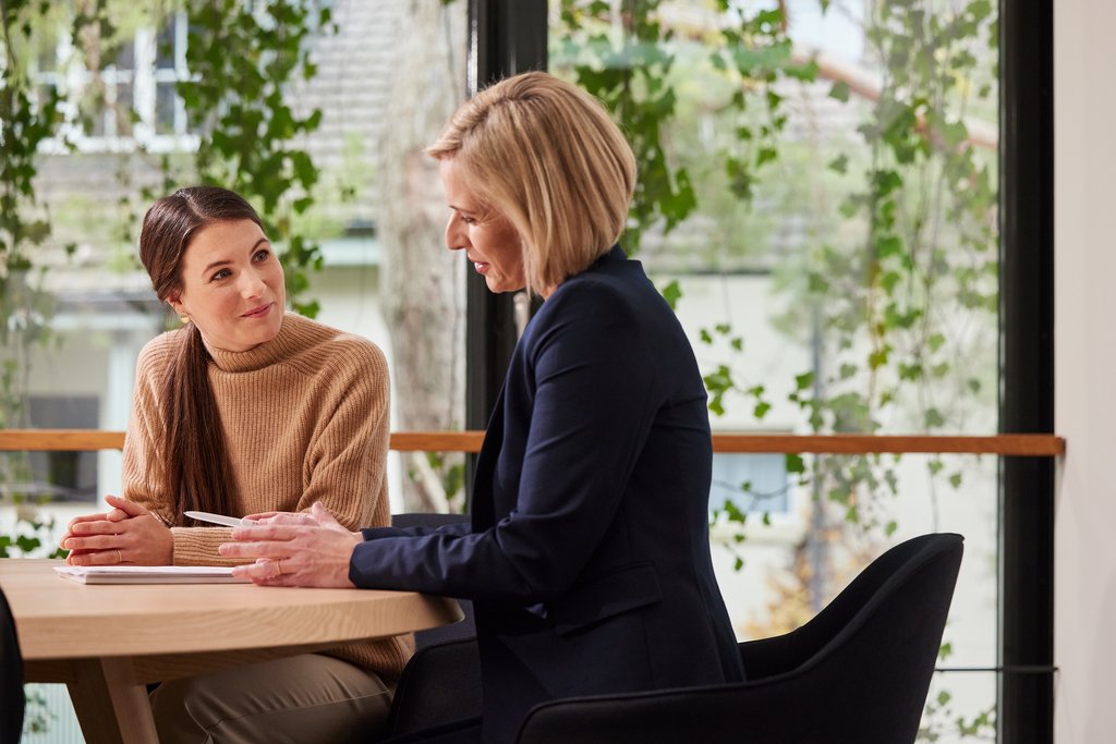 Zwei Frauen im Gespräch bei natürlichem Licht und grünem Hintergrund in einer modernen Umgebung.