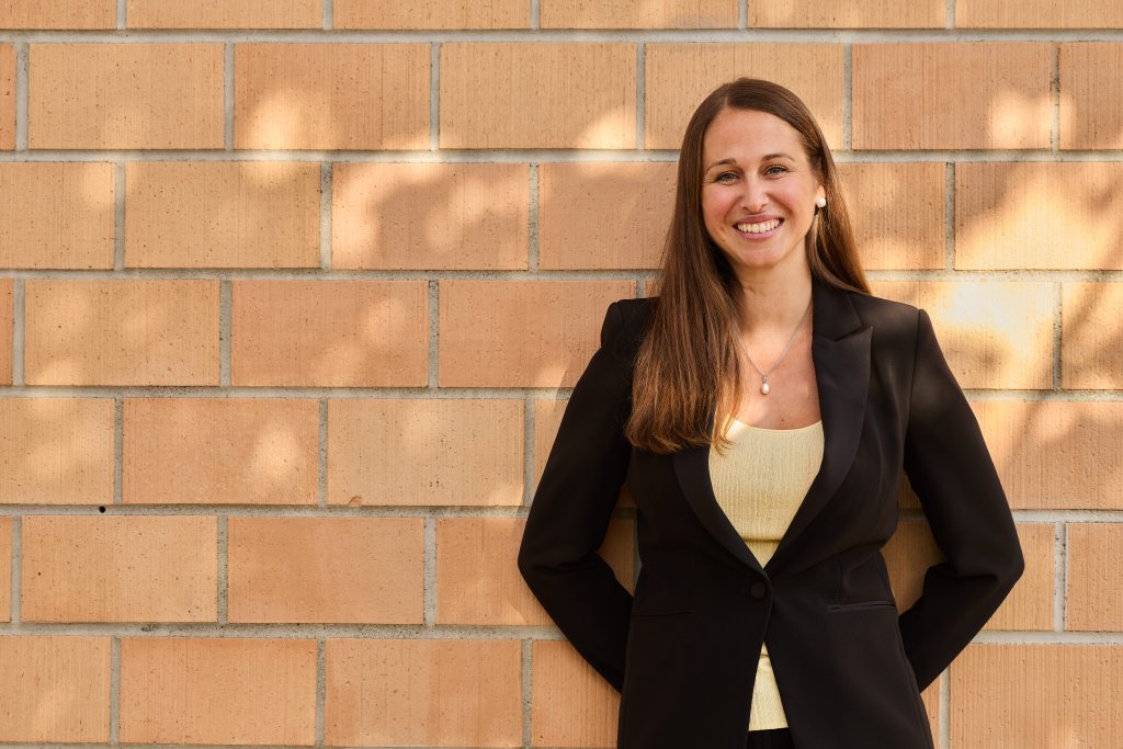 Carmen Dörfliger steht vor einer Ziegelwand, trägt Businesskleidung und schaut nach rechts.