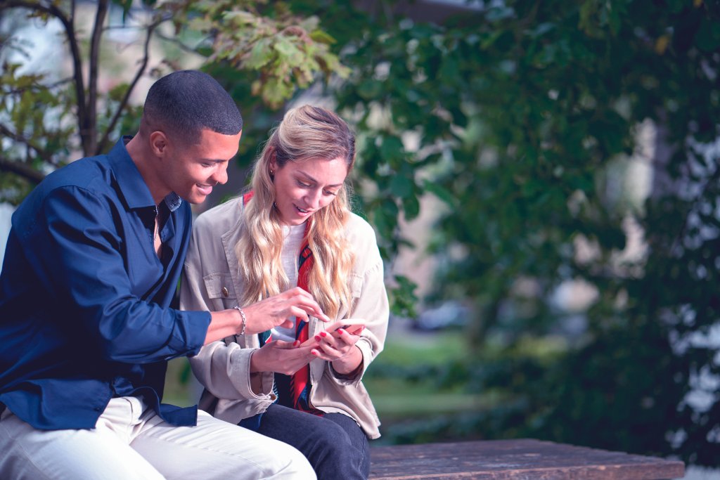 Junges Paar sitzt im Park und schaut gemeinsam auf ein Handy