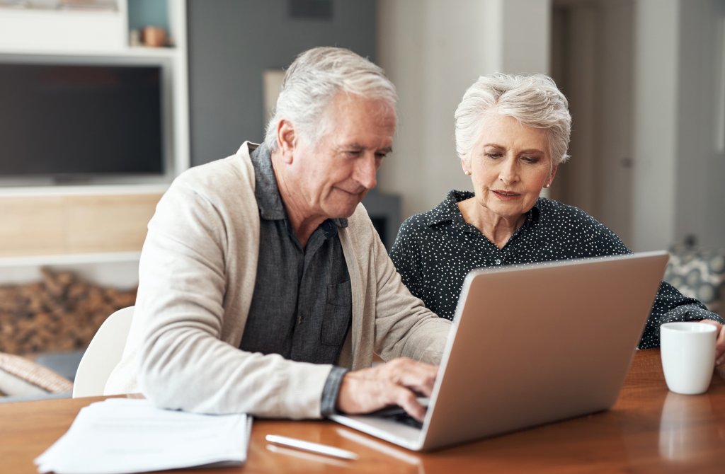 Altes Paar arbeitet zusammen an einem Laptop zu Hause, teilt Ideen und genießt ihre Zeit.