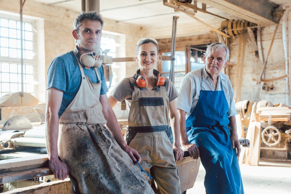 Handwerker in einer Werkstatt, lächelnd, mit Werkzeugen und Arbeitskleidung.