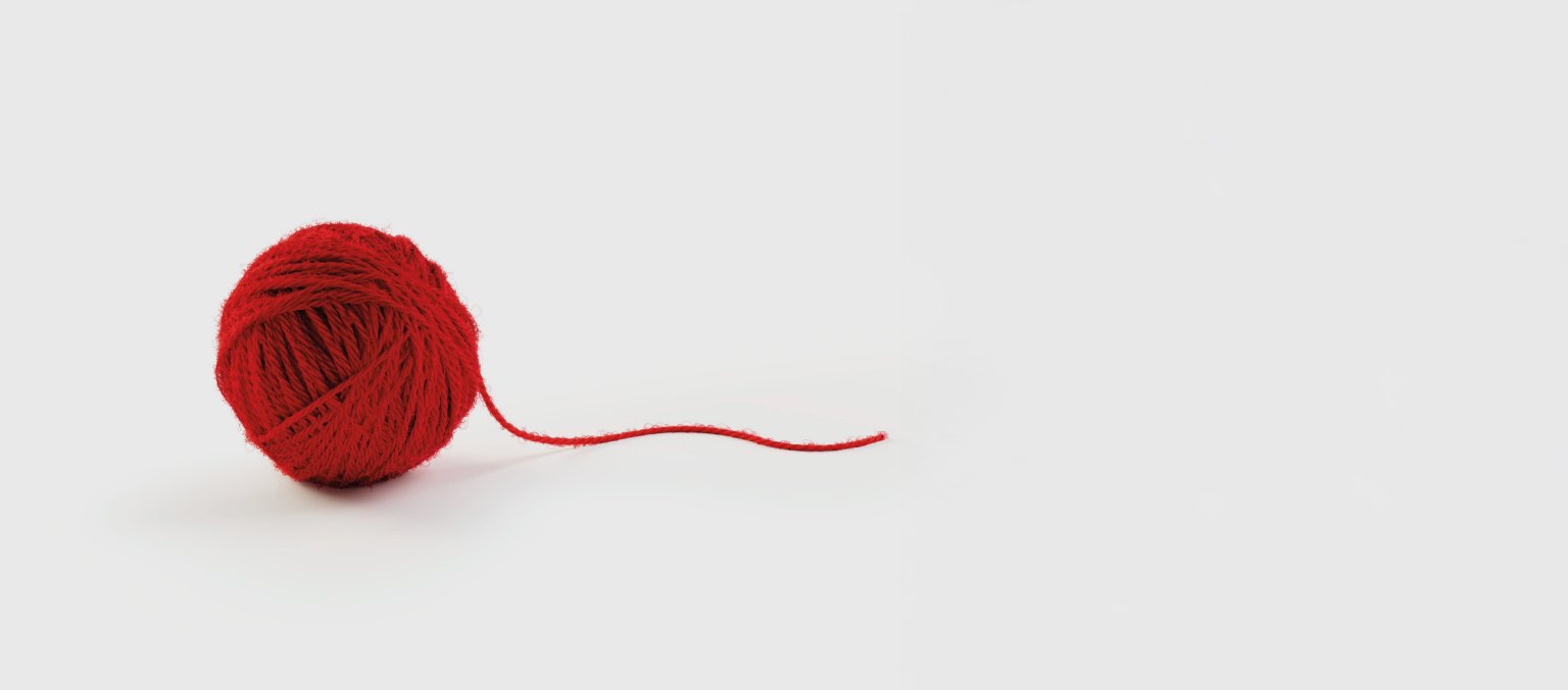 Ein roter Wollknäuel mit losem Faden auf weißem Hintergrund.