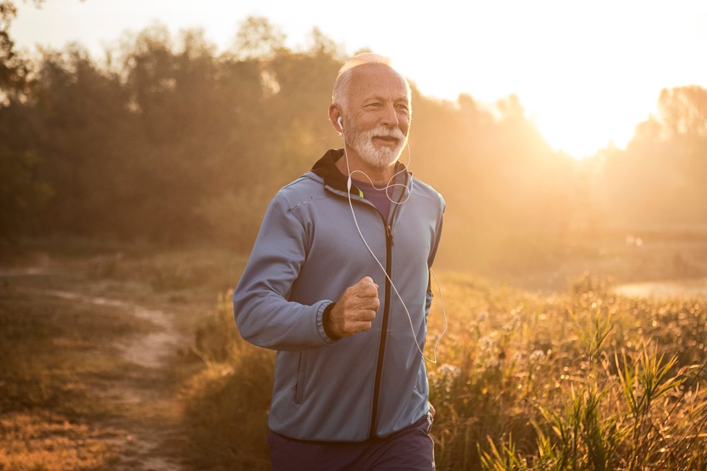 Mensch läuft joggend bei Sonnenaufgang in der Natur, trägt Kopfhörer und Jacke