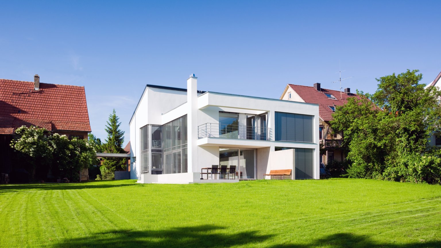 Moderne Architektur, nachhaltiges grünes Hauspanorama mit Sommergartenwiese im Vorgarten unter blauem, wolkenlosem Sommerhimmel.