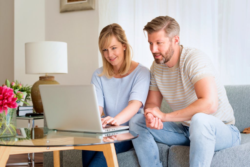 Ein Mann und eine Frau schauen gemeinsam auf einen Laptop im Wohnzimmer.