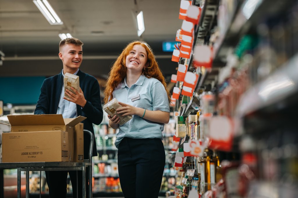 Zwei Menschen beim Einkaufen im Supermarkt, einen mit Getränke, die andere mit Geld.