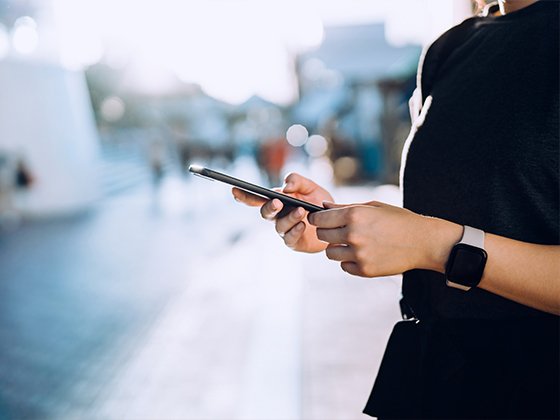 Eine junge Frau welche auf der Strasse steht und auf ihrem Smartphone etwas sucht.