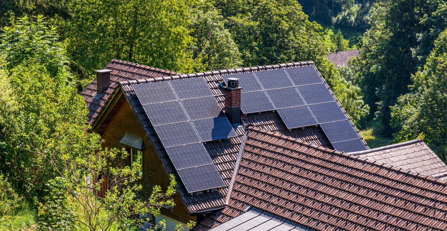 Dach mit Solarmodulen auf einem Haus in einer grünen, bewaldeten Umgebung.