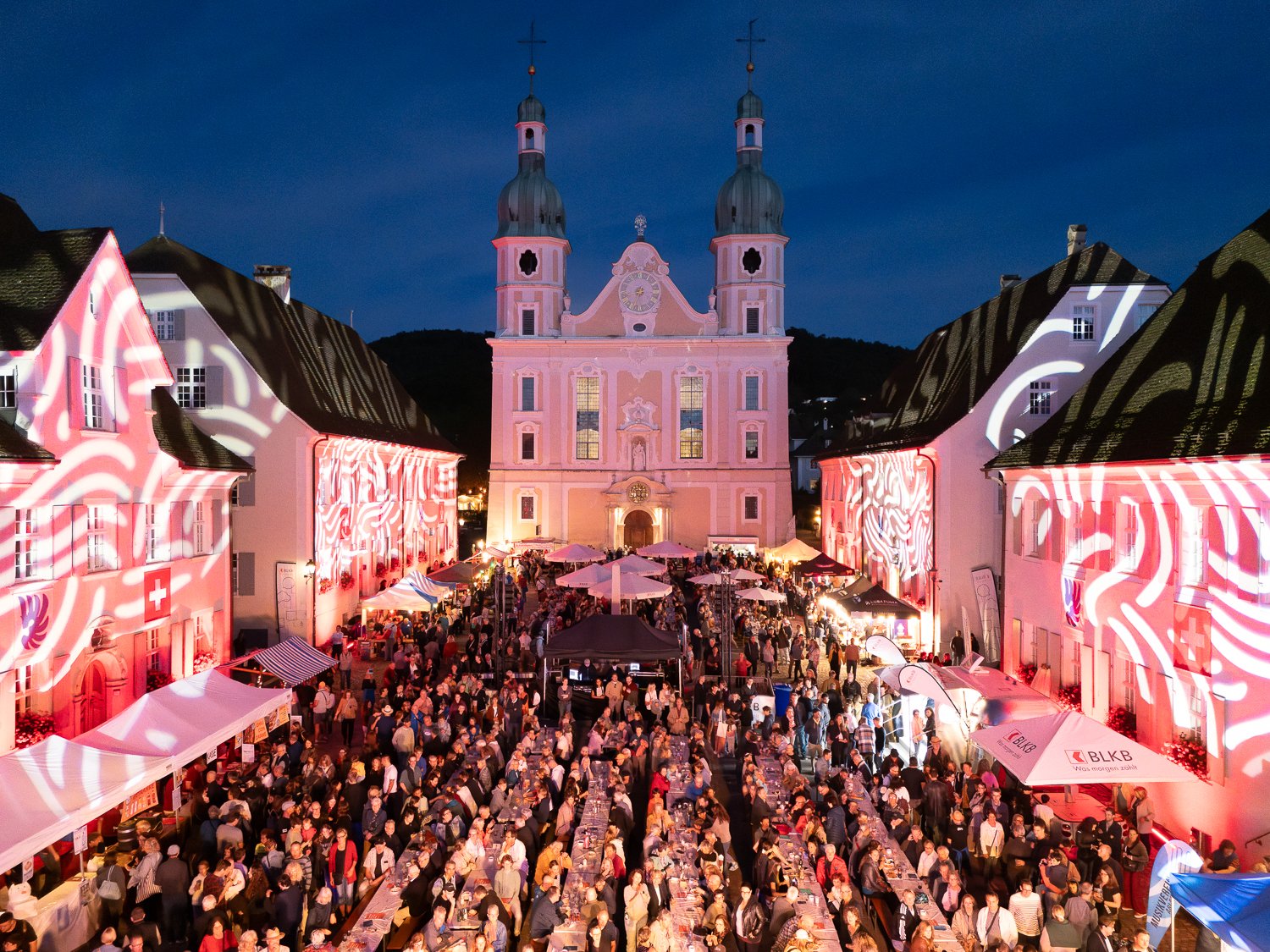 Festliches Stadtfest vor einer historischen Kirche mit vielen Besuchern und bunten Lichtern.
