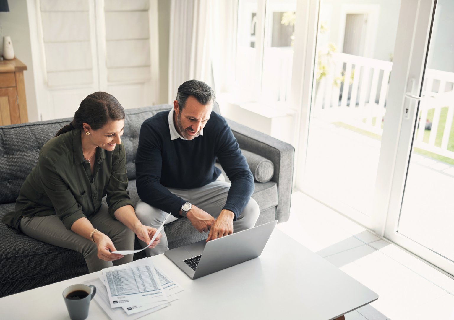 Zwei Personen arbeiten am Laptop mit Dokumenten in einem hellen Wohnzimmer