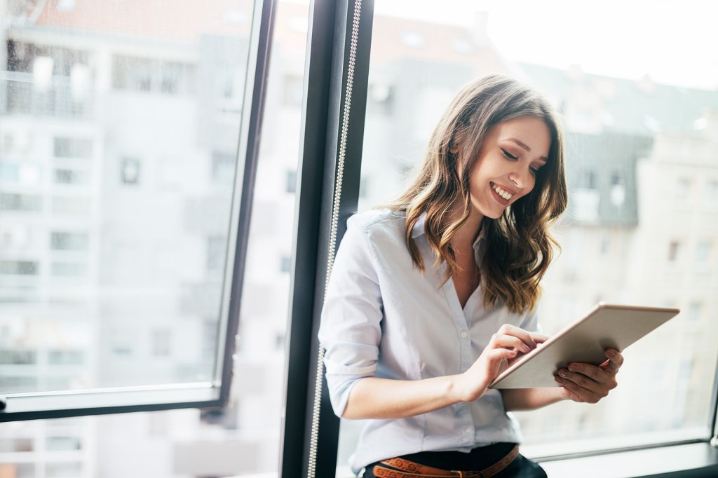 Junge Geschäftsfrau, die ein digitales Tablet benutzt, während sie vor den Fenstern im Büro steht.