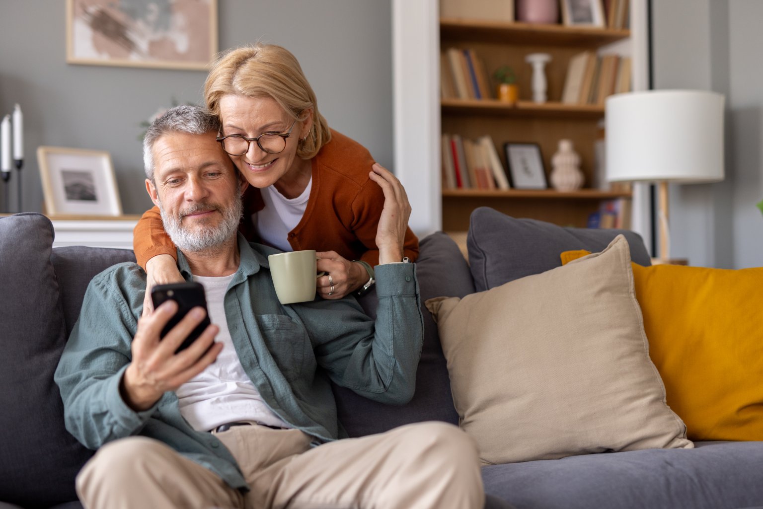 Ein Mann und eine Frau sitzen auf einem Sofa, schauen auf ein Smartphone. aus dem Artikel Wohnen im Alter: Frühzeitig die richtigen Weichen stellen