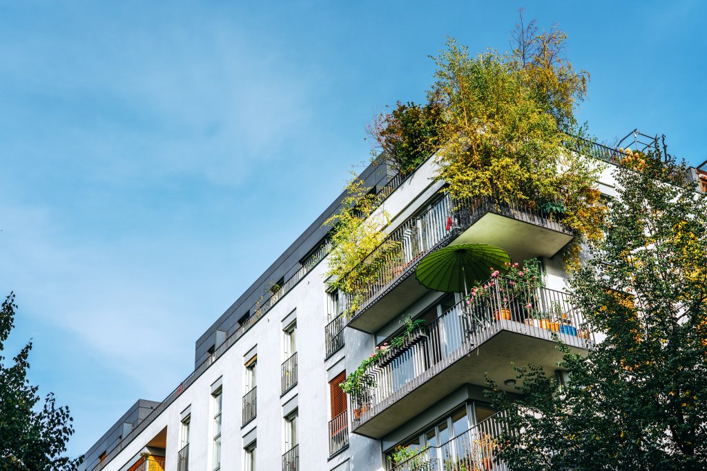 Mehrfamilienhaus mit zwei bepflanzten Balkonen. Auf einem der Balkone steht ein auffällig grüner Sonnenschirm.