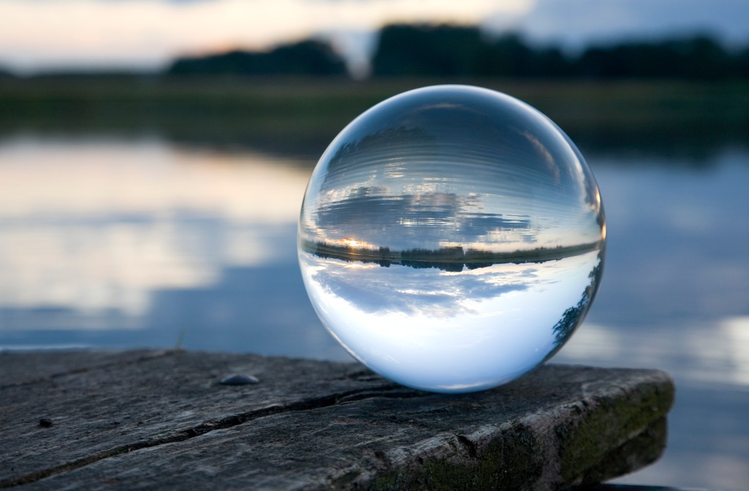 Eine Glasskugel auf einer Holzoberfläche vor einem ruhigen Fluss mit Baumhimmelreflexion. aus dem Artikel Rückenwind für die Schwellenländer hält an