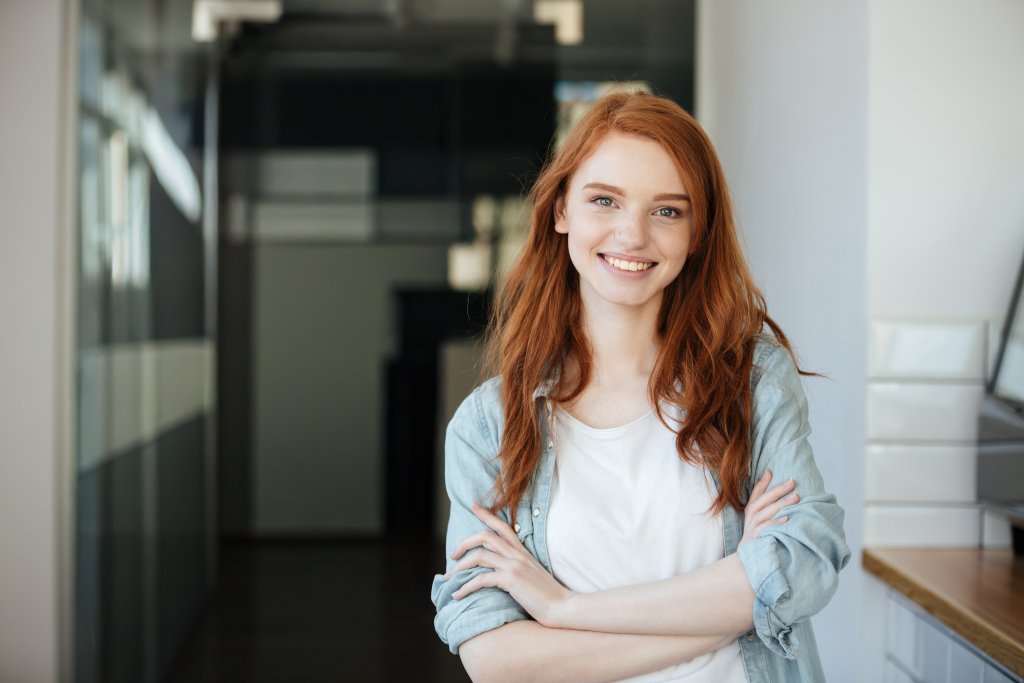 Eine junge Frau mit roten Haaren steht in einem modernen Raum mit weißen Wänden.