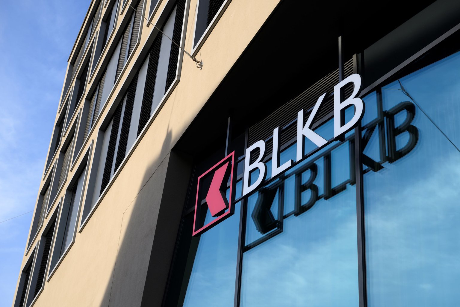 Gebäudefront mit Logo der Basellandschaftlichen Kantonalbank BLKB  und reflektierende Glasscheibe.