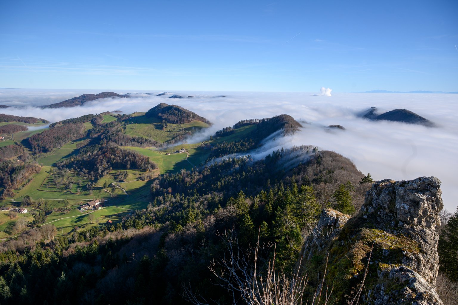Berglandschaft mit Wolken, Grüntäler und Felsen im Vordergrund bei schönem Himmel