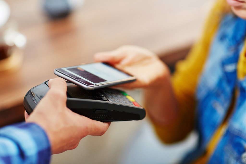 Nahaufnahme einer Frau, die ihre Bestellung an einem Zahlterminal mit ihrem Smartphone bezahlt.