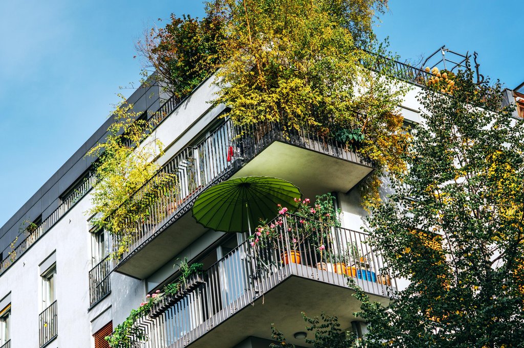 Mehrfamilienhaus mit zwei bepflanzten Balkonen. Auf einem der Balkone steht ein auffällig grüner Sonnenschirm.