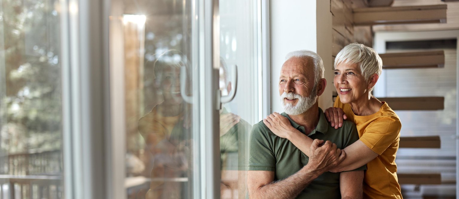 Zwei Personen umarmen sich freundlich hinter einem grossen Fenster.