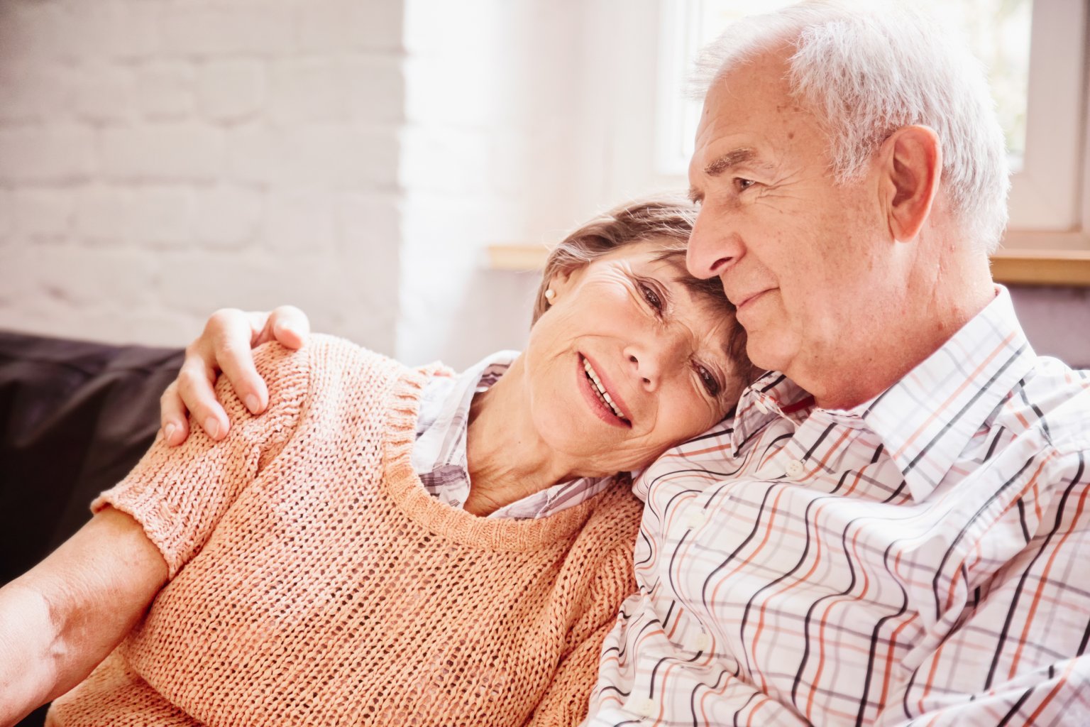 An older woman lies on a man, both smile kindly in the bright room.