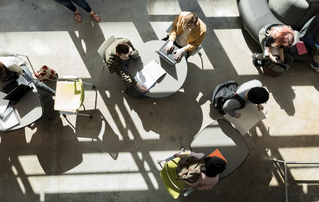 Eine Draufsicht auf eine multiethnische Gruppe von College-Studenten, die in der Lobby des Unterrichtsgebäudes an verschiedenen Projekten und Hausaufgaben arbeiten.
