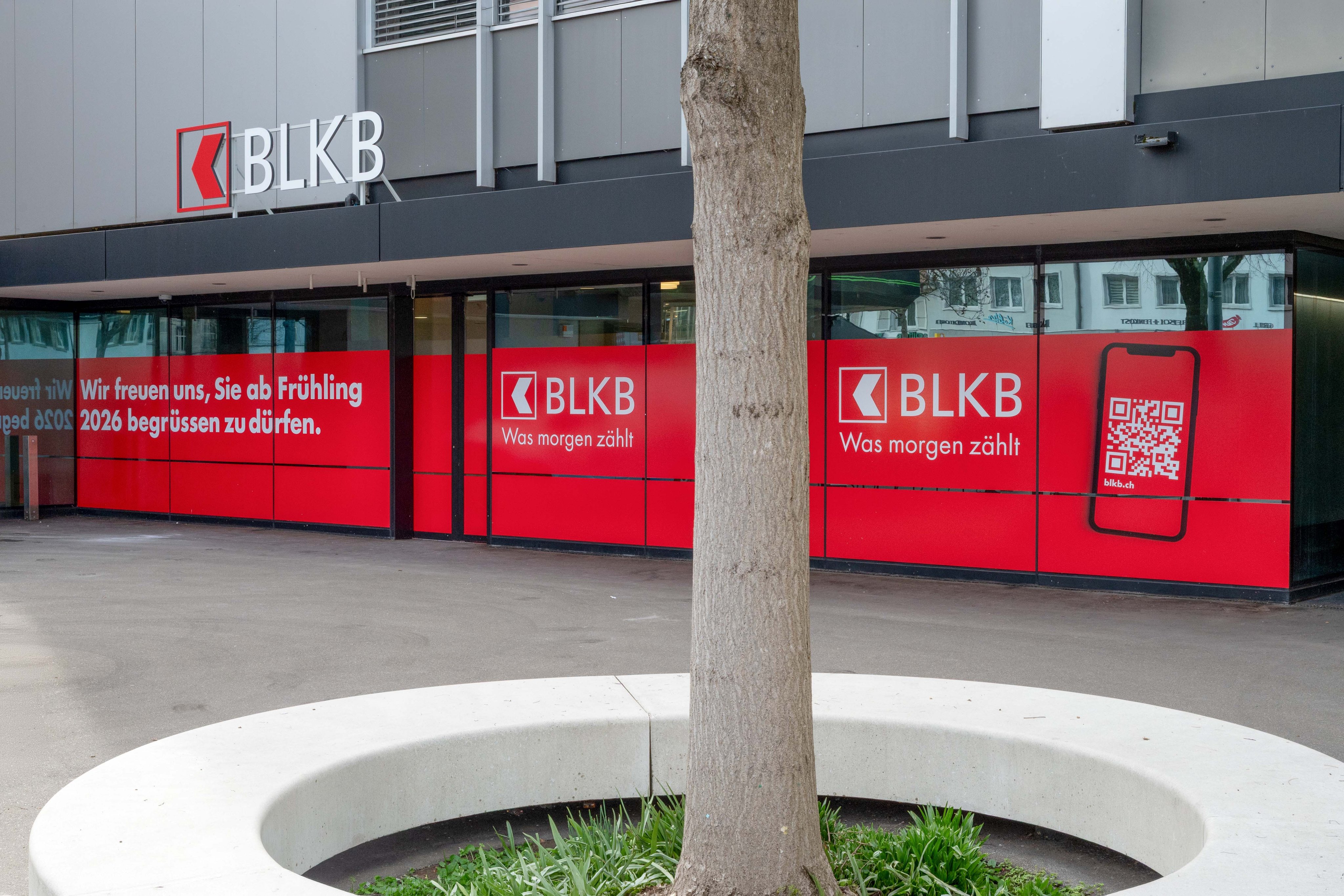 Fensterfront mit roten Werbebanner der BLKB-Niederlassung in Reinach und QR-Code zu blkb.ch.