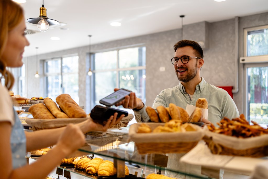 Kunde kauft Bäckereiwaren und nutzt moderne Zahlungsmethoden in einem einladenden Geschäft.