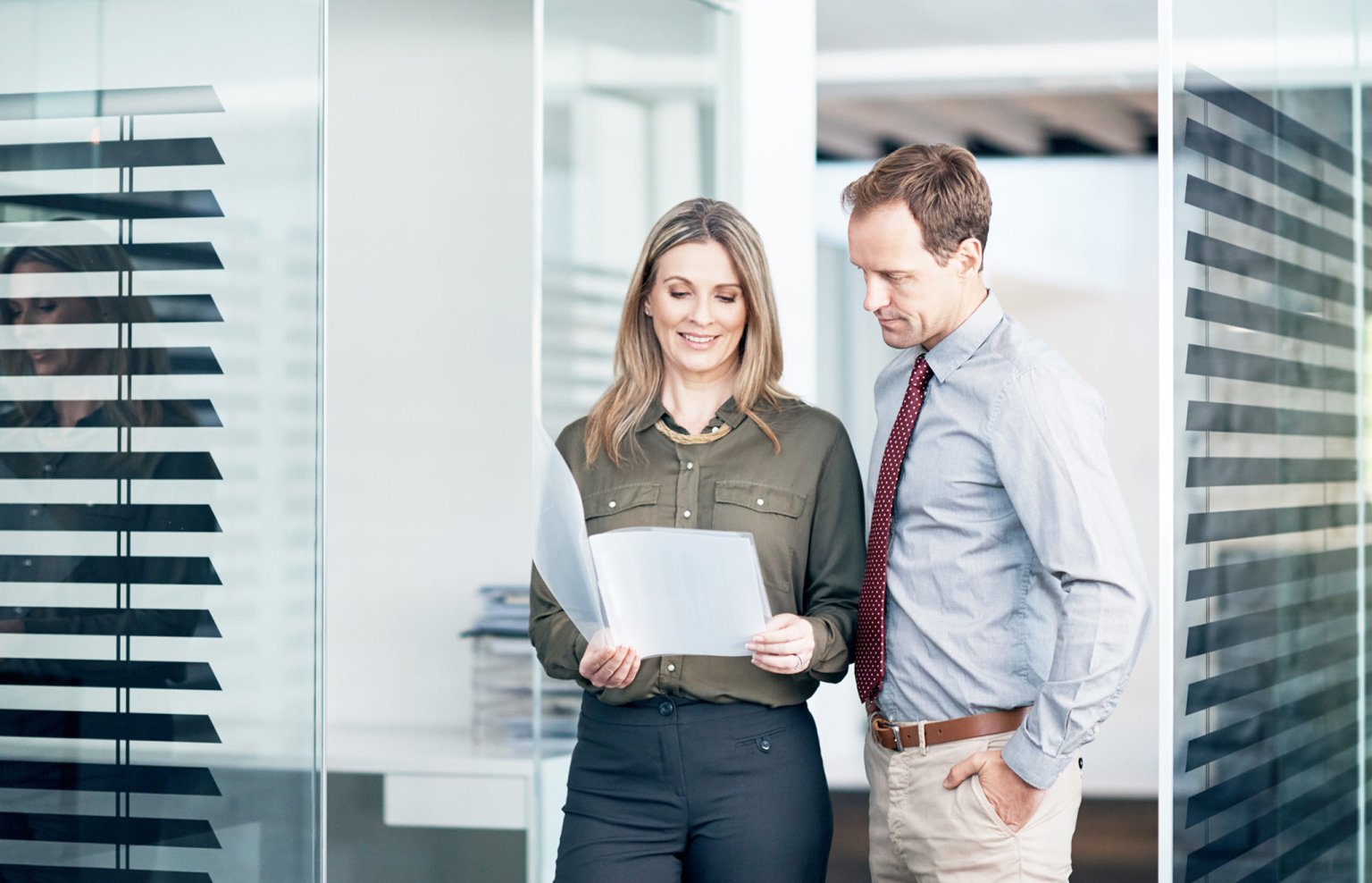 Zwei Personen in einem modernen Bürolokal betrachten Dokumente miteinander.