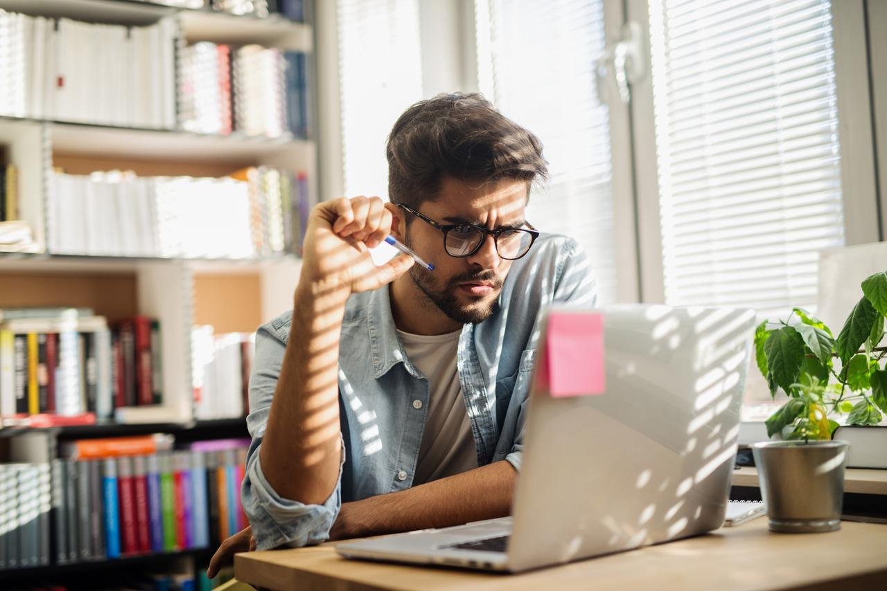 Mann mit einem Stift sitzt am Schreibtisch einer Bibliothek und schaut etwas auf seinem Laptop. aus dem Artikel Anlagefonds sind aktuell sehr beliebt – zu Recht?