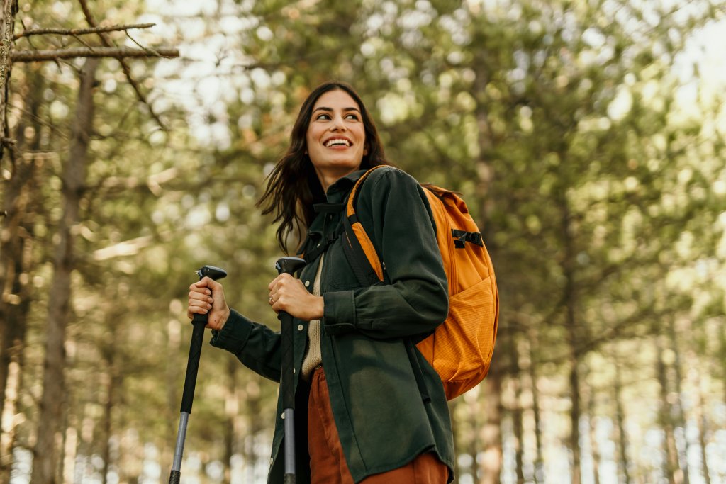 Frau mit Rucksack wandert gemütlich durch den Wald an einem sonnigen Tag.