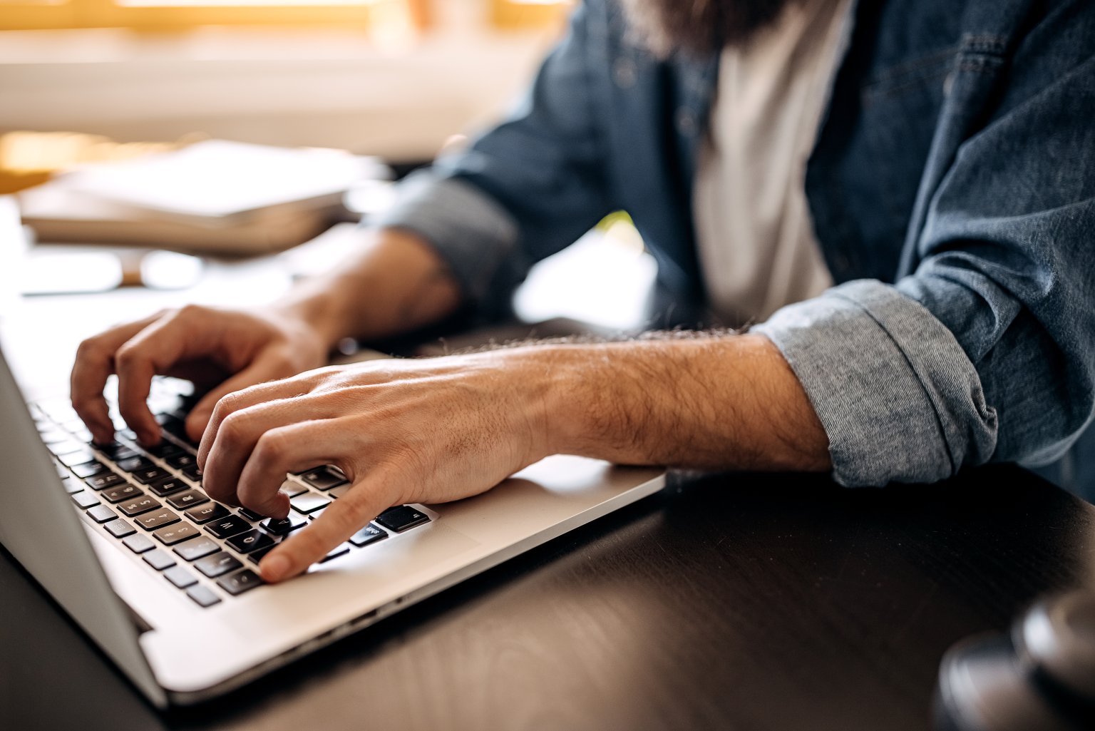 Eine Mann, der mit Fokus und Konzentration auf einer Laptop-Tastatur tippt.