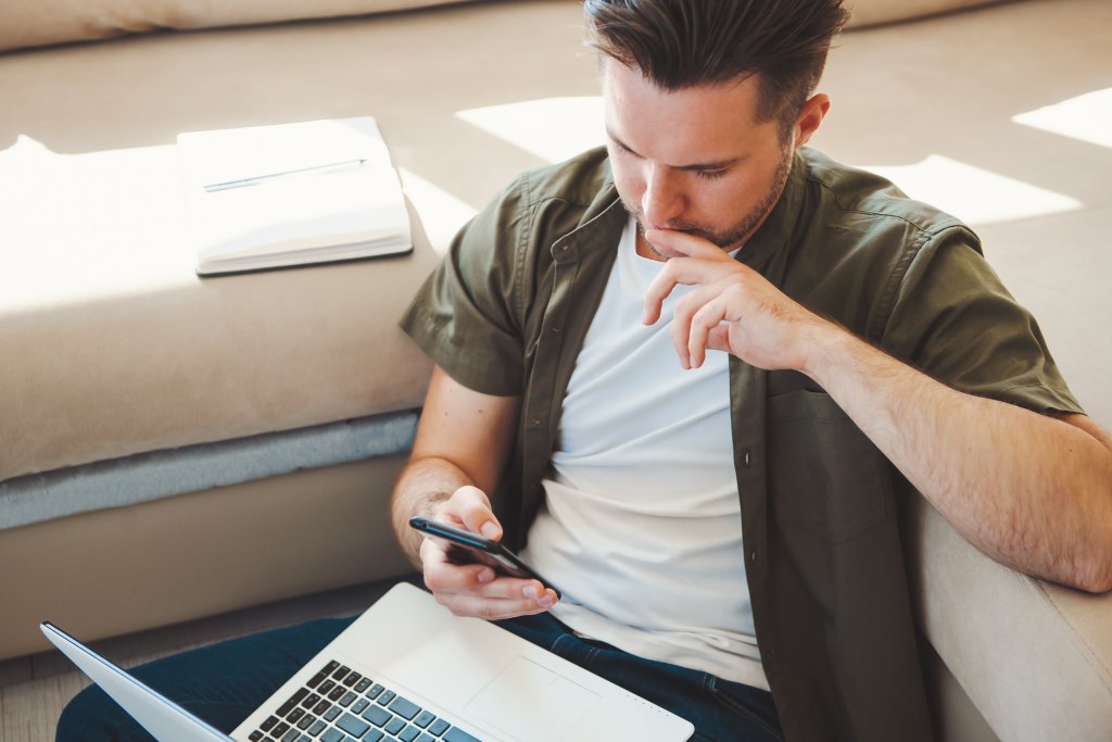 Mann nutzt Smartphone und Laptop in einer entspannten Umgebung.