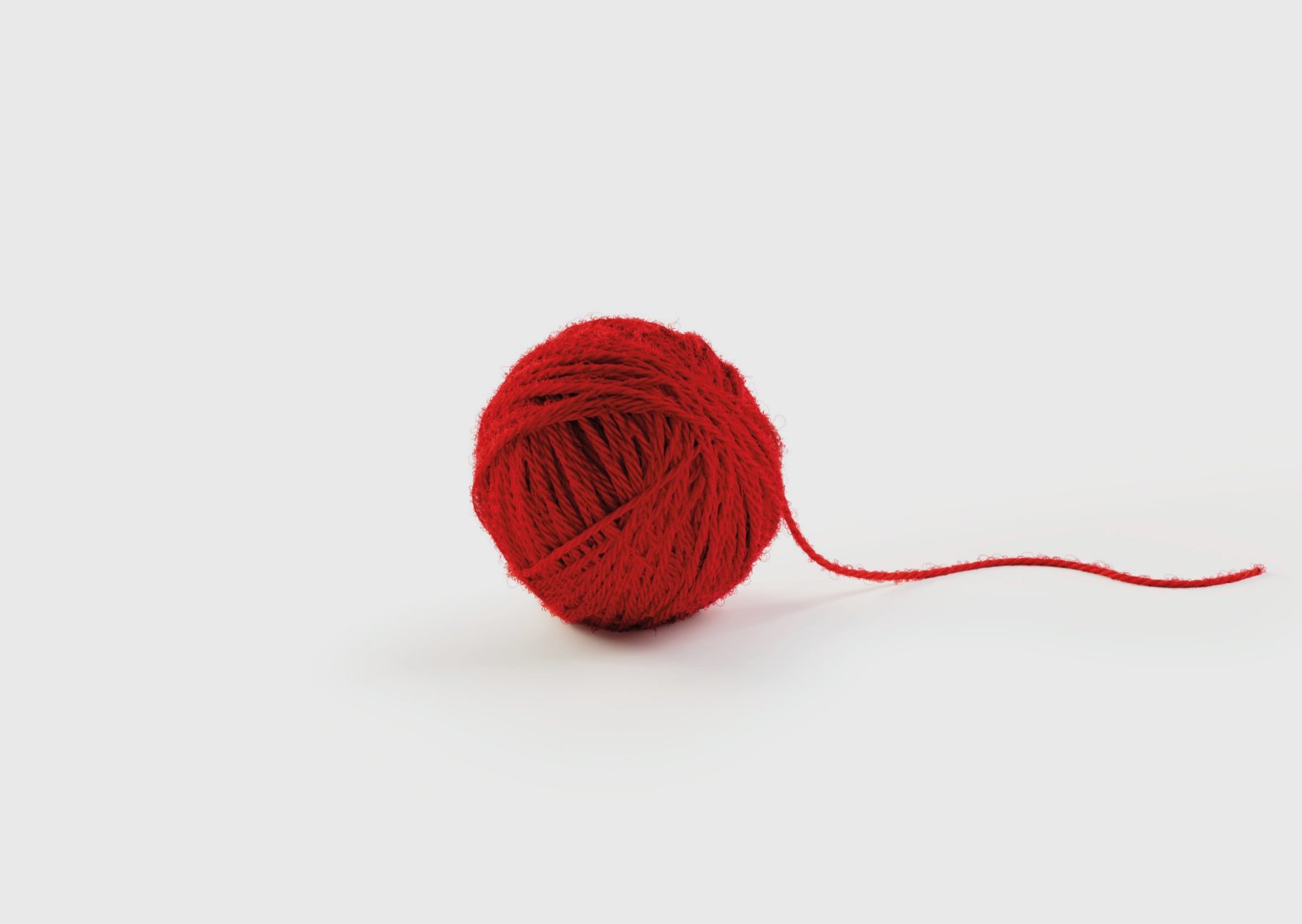 Ein roter Wollknäuel mit losem Faden auf weißem Hintergrund