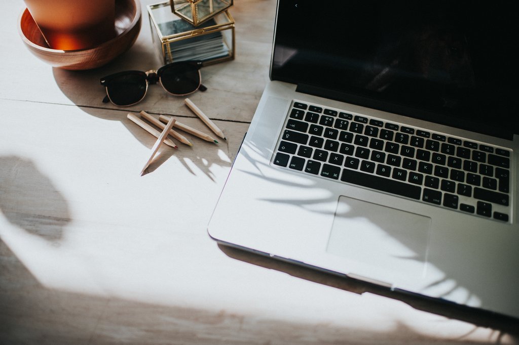 Schreibtisch mit Laptop, Sonnenbrille und Bürobedarf in hellem, natürlichem Licht.