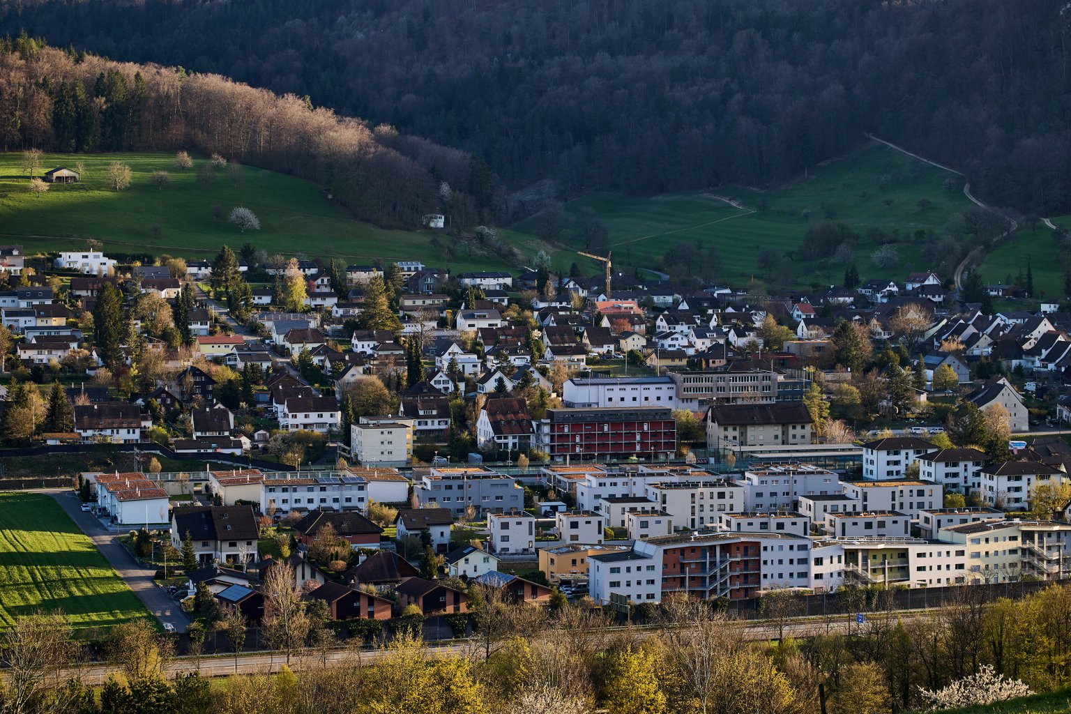 Blick auf eine Stadt in einer bergigen Landschaft, mit Gebäuden und grünen Flächen.