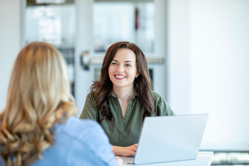 Zwei Frauen im Gespräch an einem Tisch, im Hintergrund Büroatmosphäre bei BLKB