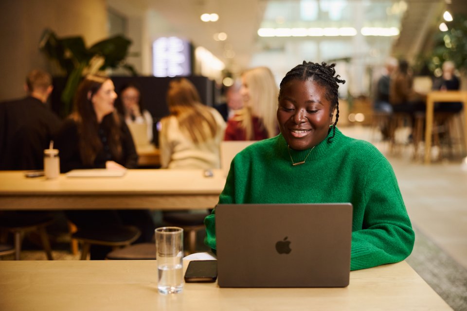 A woman at a laptop with people working in the background