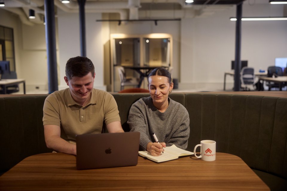 A group of people sat on wooden seating enjoying food and drinks