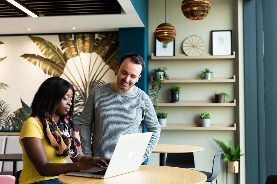 A woman at a laptop with a man stood with her